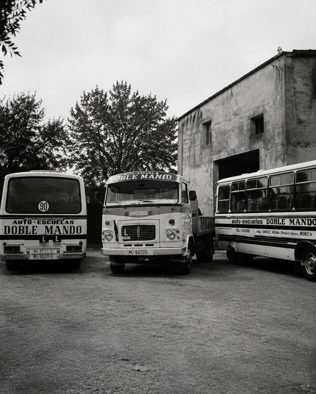 Fotografía histórica en blanco y negro: un camión y dos autobuses de prácticas rotulados «Auto-Escuelas Doble Mando»
